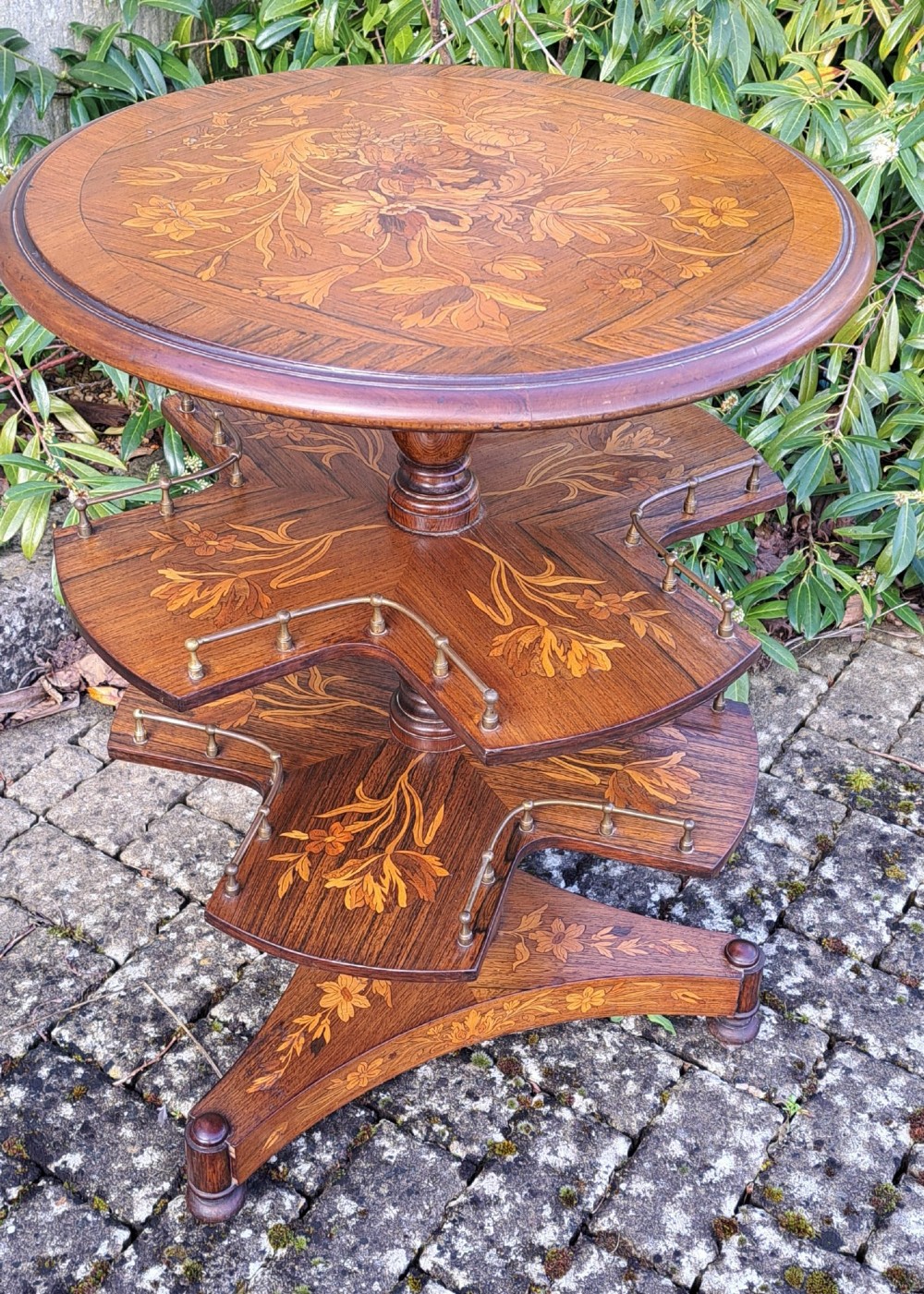 A circular Dutch marquetry revolving library table with floral wood inlays, tiered shelves featuring brass galleries, and a quadform pedestal base. View VII