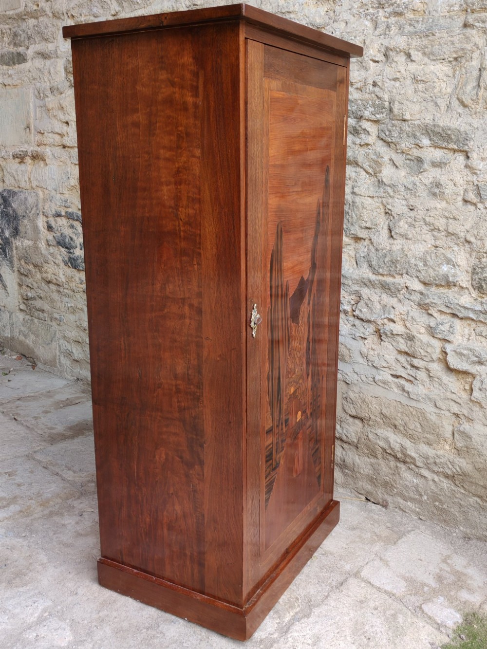 A tall mahogany single-door cupboard featuring a prominent marquetry inlaid panel depicting a mountain landscape with tall trees and a central path. View III