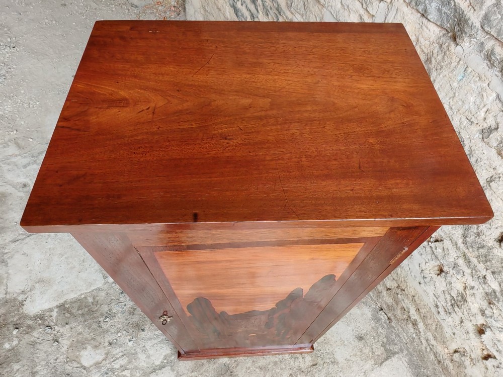A tall mahogany single-door cupboard featuring a prominent marquetry inlaid panel depicting a mountain landscape with tall trees and a central path. View IV