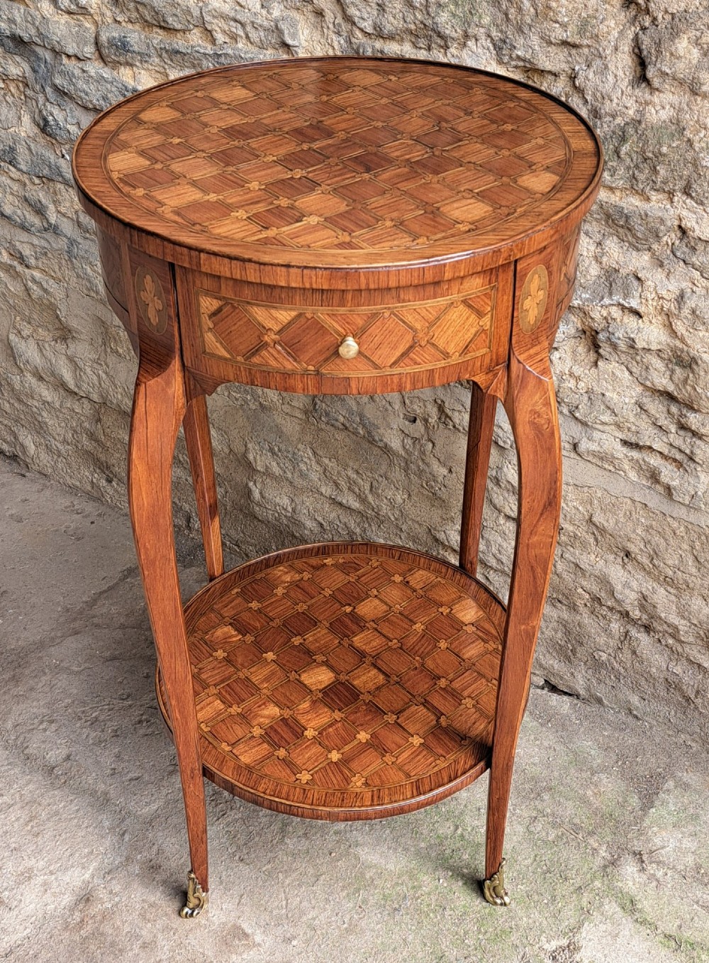 An antique circular French kingwood two-tier occasional table with geometric parquetry inlay, cabriole legs, and brass sabots.