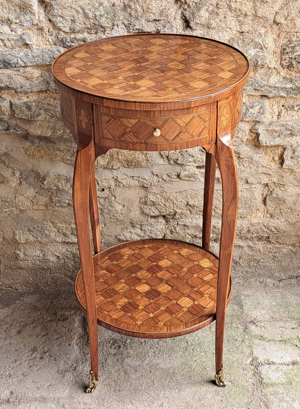 An antique circular French kingwood two-tier occasional table with geometric parquetry inlay, cabriole legs, and brass sabots. View II