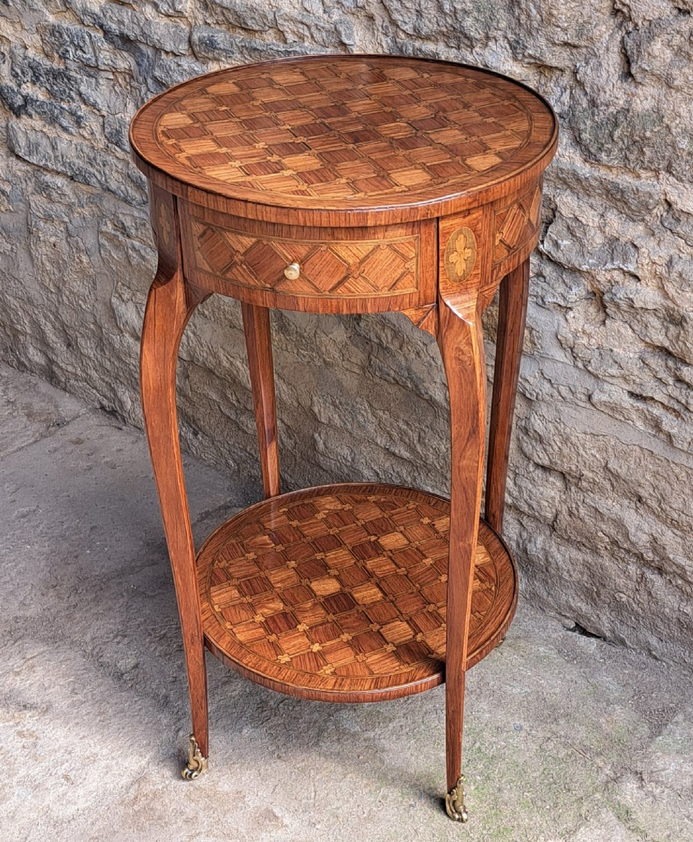 An antique circular French kingwood two-tier occasional table with geometric parquetry inlay, cabriole legs, and brass sabots. View X