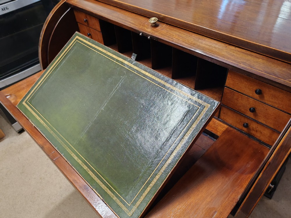 A Georgian mahogany cylinder top desk featuring a curved roll lid, inlaid detailing, multiple drawers with brass handles, pull-out side slides, and spiral turned legs on brass castors. View VII