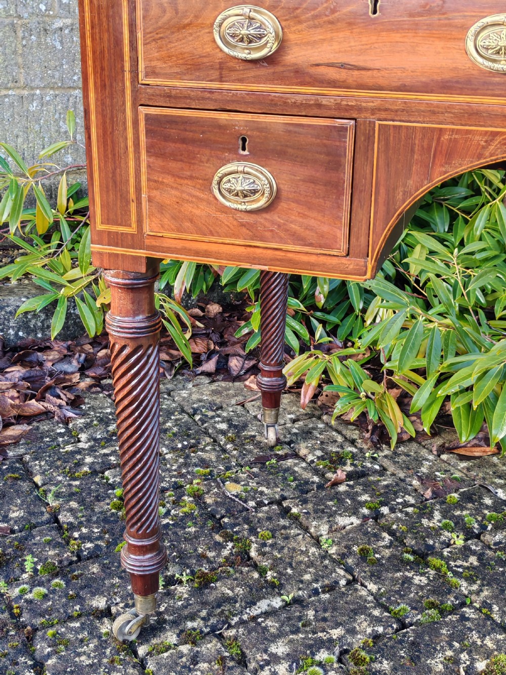 A Georgian mahogany cylinder top desk featuring a curved roll lid, inlaid detailing, multiple drawers with brass handles, pull-out side slides, and spiral turned legs on brass castors. View IX