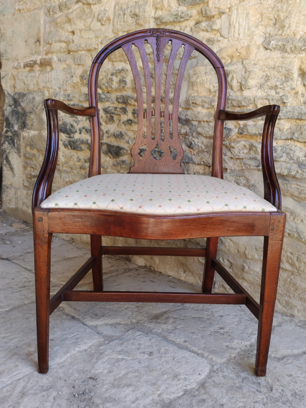 An 18th-century mahogany Hepplewhite carver armchair featuring an arched back with a pierced splat, sweeping armrests, an patterned upholstered seat, and square tapered legs. View IV