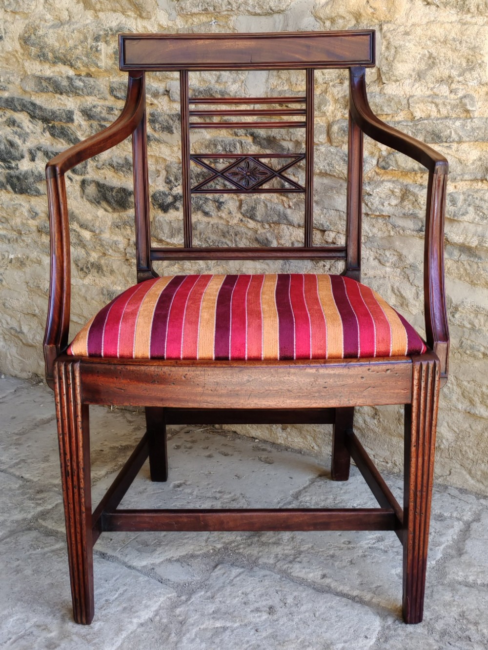 A late 18th-century Georgian mahogany carver chair featuring curved armrests, a carved diamond back splat, reeded front legs, and a red-striped upholstered seat.