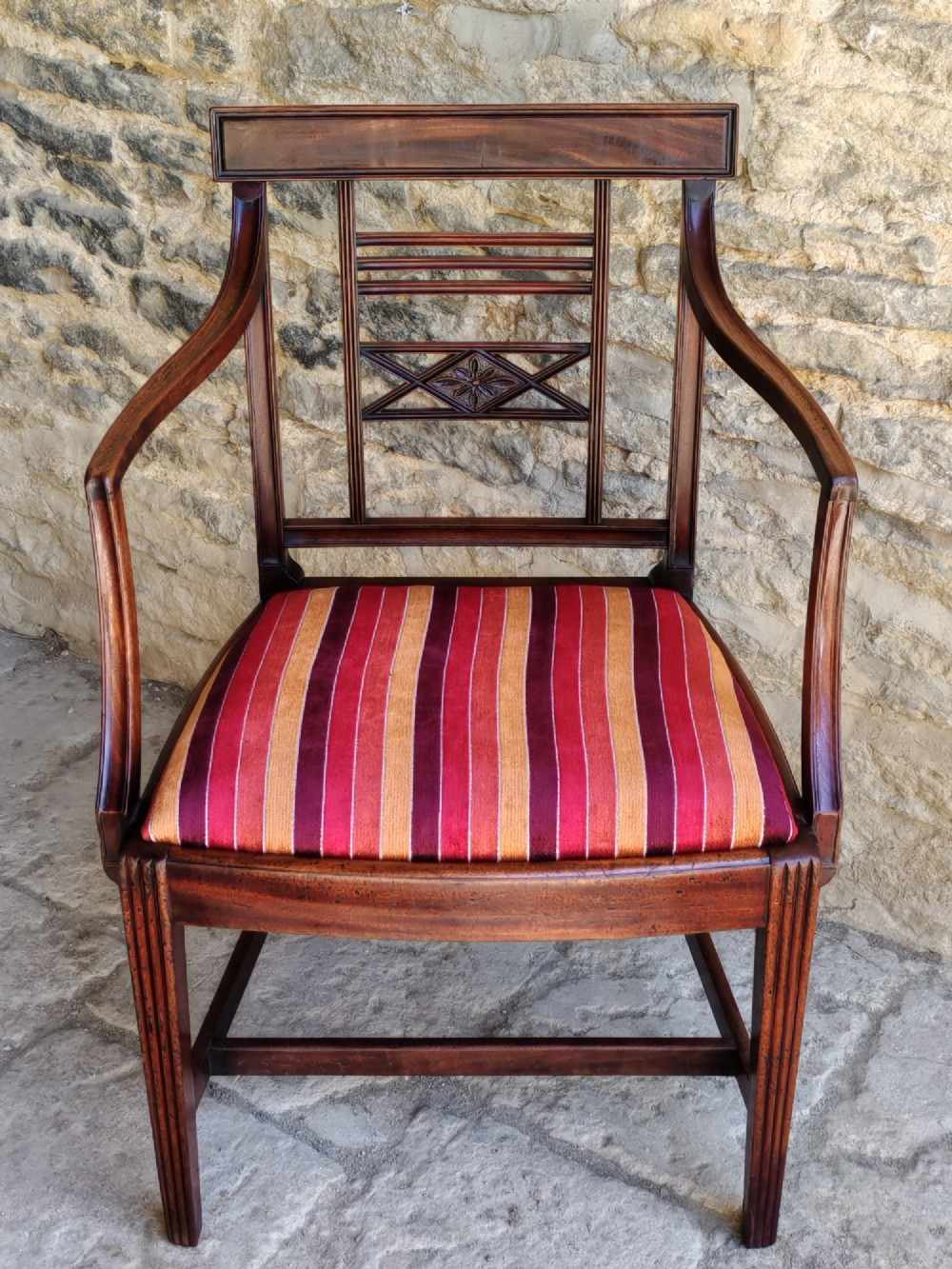 A late 18th-century Georgian mahogany carver chair featuring curved armrests, a carved diamond back splat, reeded front legs, and a red-striped upholstered seat. View II