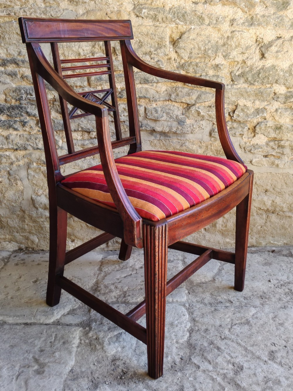 A late 18th-century Georgian mahogany carver chair featuring curved armrests, a carved diamond back splat, reeded front legs, and a red-striped upholstered seat. View III