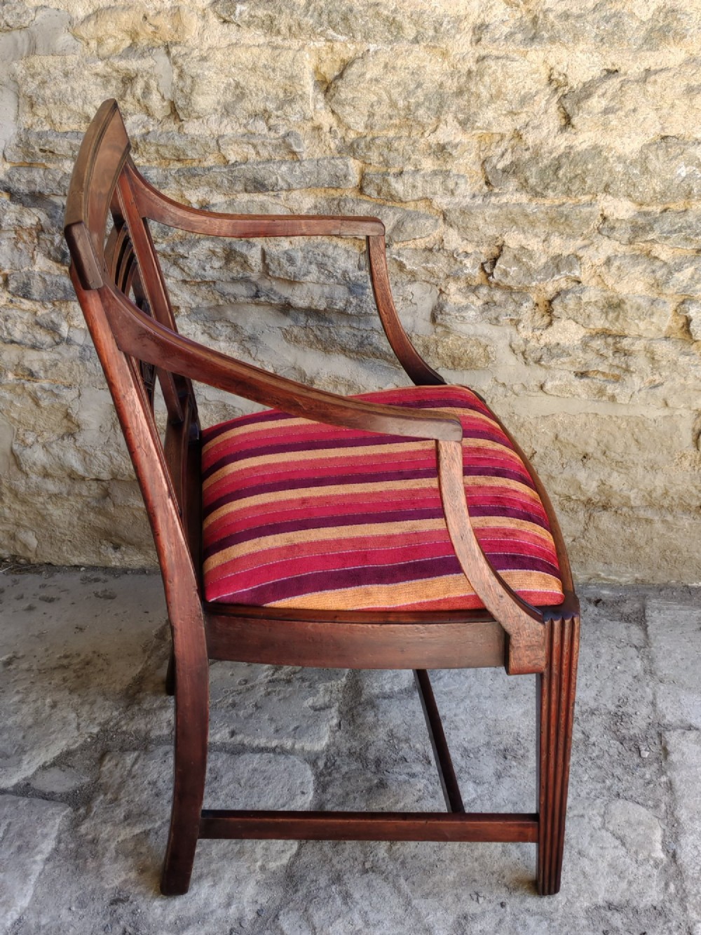 A late 18th-century Georgian mahogany carver chair featuring curved armrests, a carved diamond back splat, reeded front legs, and a red-striped upholstered seat. View IV