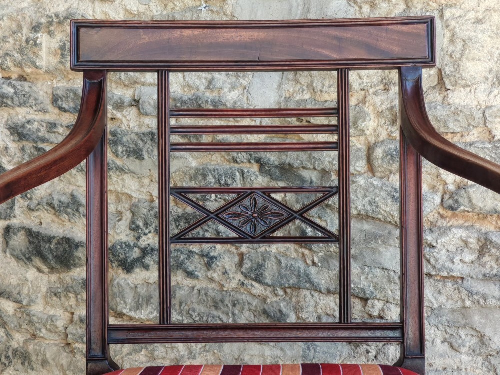 A late 18th-century Georgian mahogany carver chair featuring curved armrests, a carved diamond back splat, reeded front legs, and a red-striped upholstered seat. View V