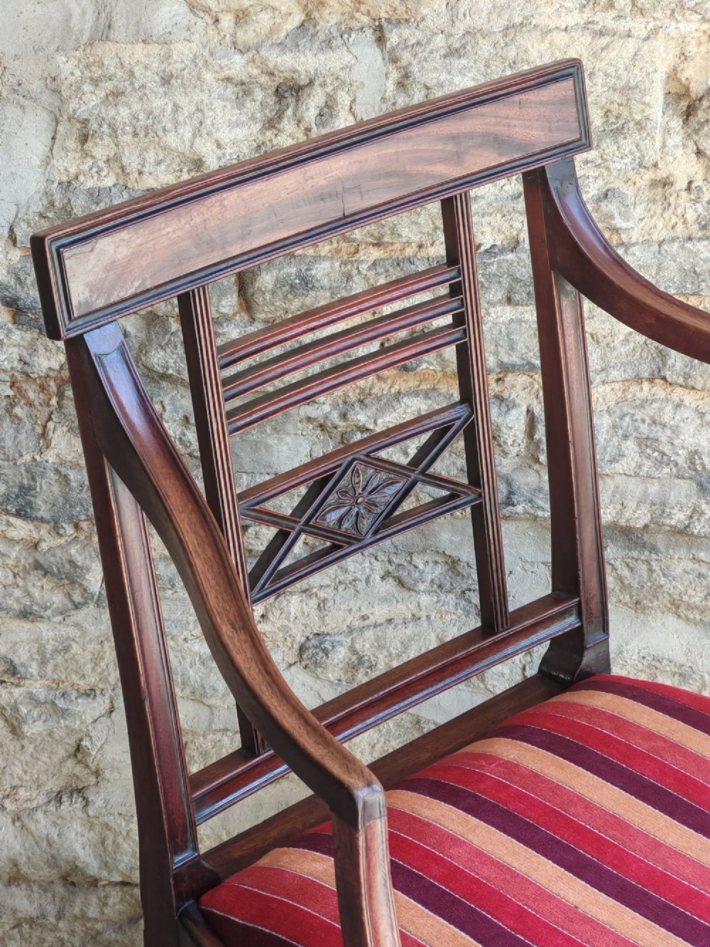 A late 18th-century Georgian mahogany carver chair featuring curved armrests, a carved diamond back splat, reeded front legs, and a red-striped upholstered seat. View VI