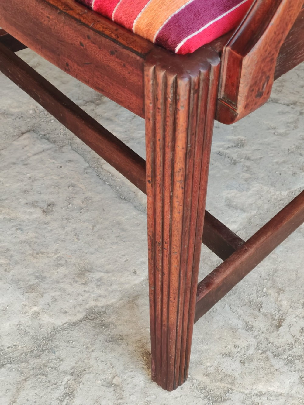 A late 18th-century Georgian mahogany carver chair featuring curved armrests, a carved diamond back splat, reeded front legs, and a red-striped upholstered seat. View IX