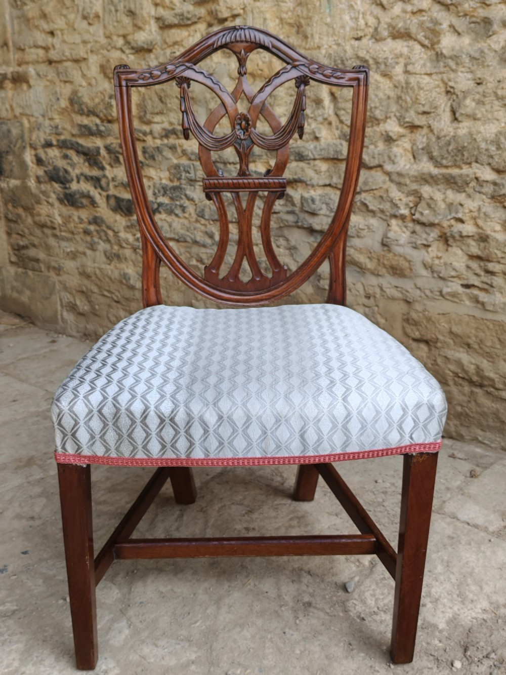 A Georgian walnut side chair featuring a carved shield backrest with openwork detailing and a patterned upholstered seat.