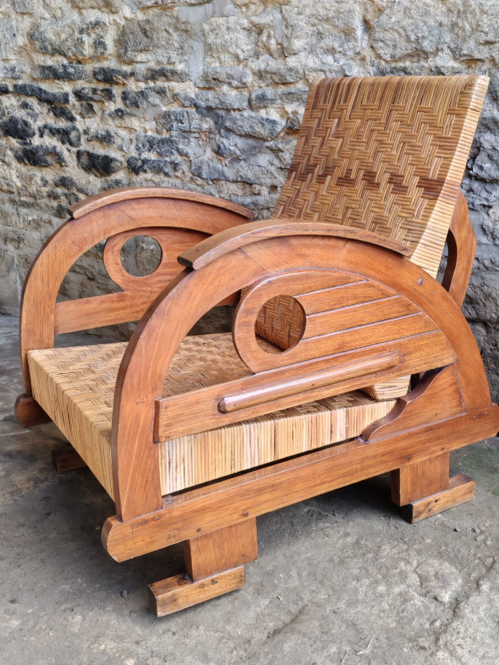 An Art Deco low-slung armchair featuring thick curved wooden armrests with circular cut-outs and a woven rattan seat and backrest. View III