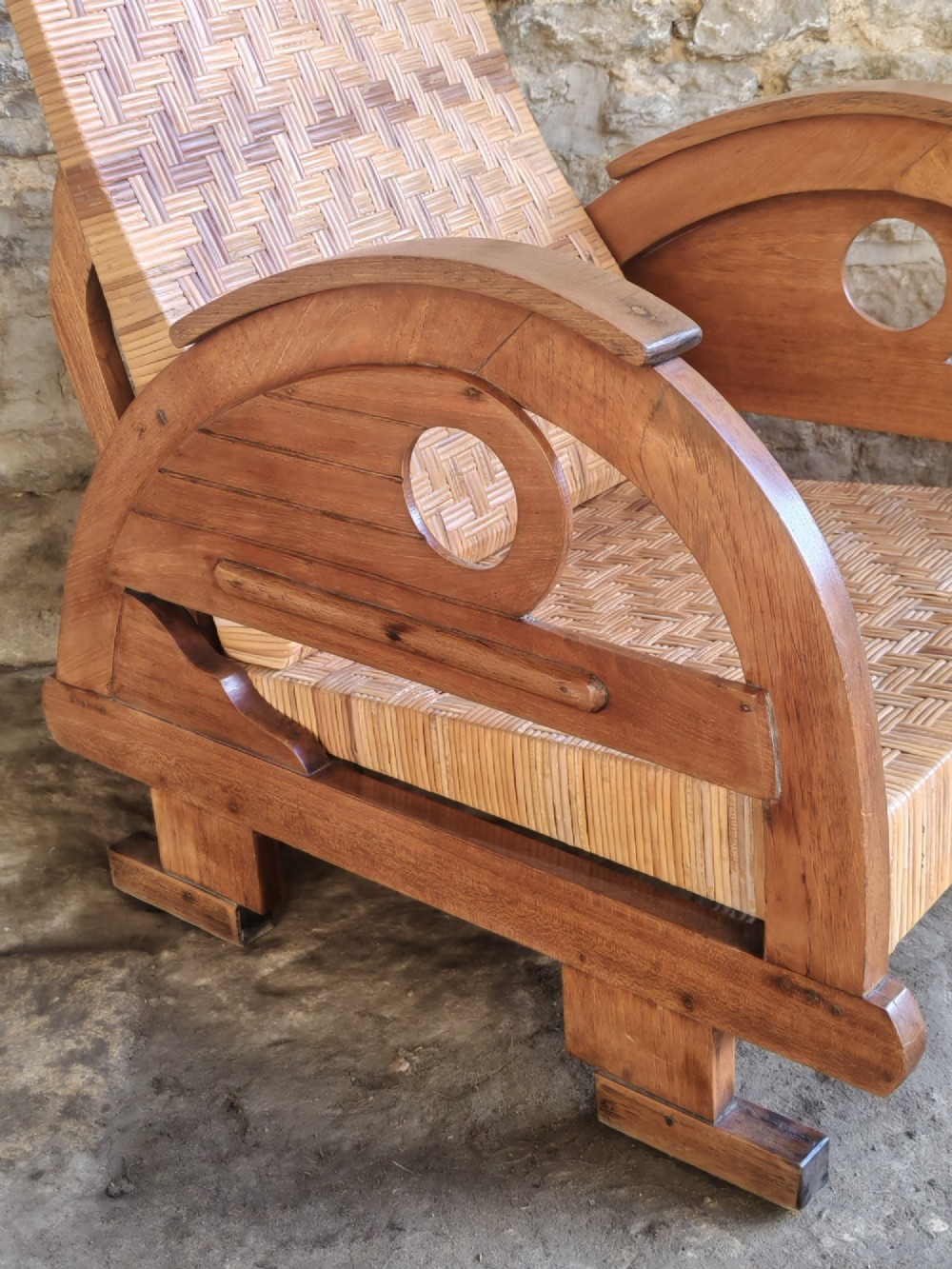 An Art Deco low-slung armchair featuring thick curved wooden armrests with circular cut-outs and a woven rattan seat and backrest. View IV