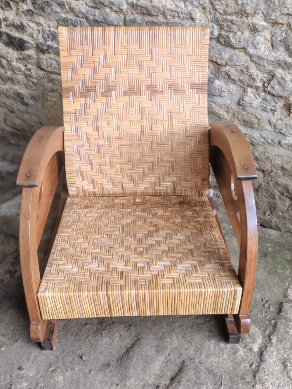 An Art Deco low-slung armchair featuring thick curved wooden armrests with circular cut-outs and a woven rattan seat and backrest. View VI