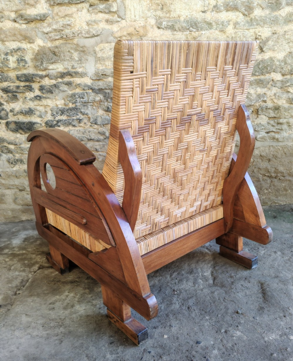 An Art Deco low-slung armchair featuring thick curved wooden armrests with circular cut-outs and a woven rattan seat and backrest. View VIII