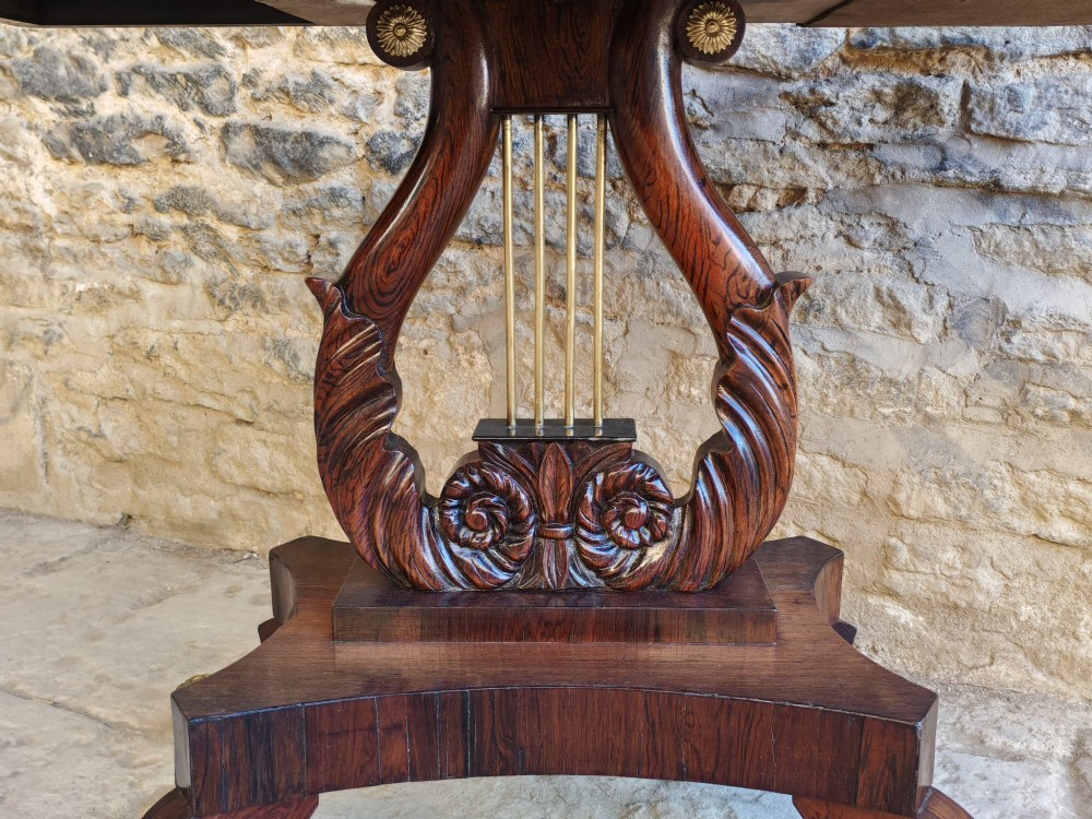 A Regency period rosewood tea table featuring a fold-over top, a central lyre-shaped support with brass rods, and a four-footed pedestal base with brass castors. View II