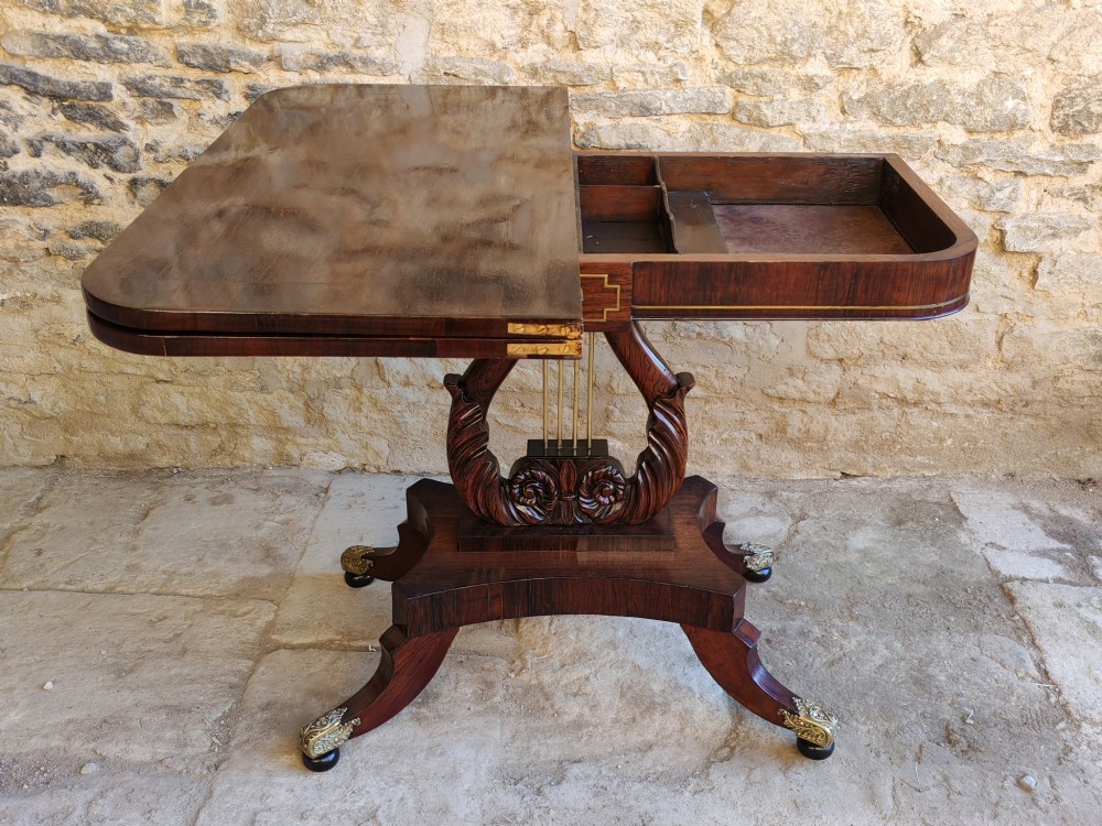 A Regency period rosewood tea table featuring a fold-over top, a central lyre-shaped support with brass rods, and a four-footed pedestal base with brass castors. View VII