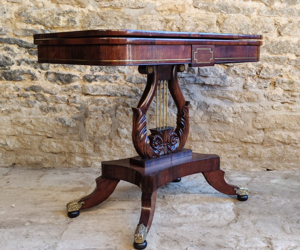 A Regency period rosewood tea table featuring a fold-over top, a central lyre-shaped support with brass rods, and a four-footed pedestal base with brass castors. View IX