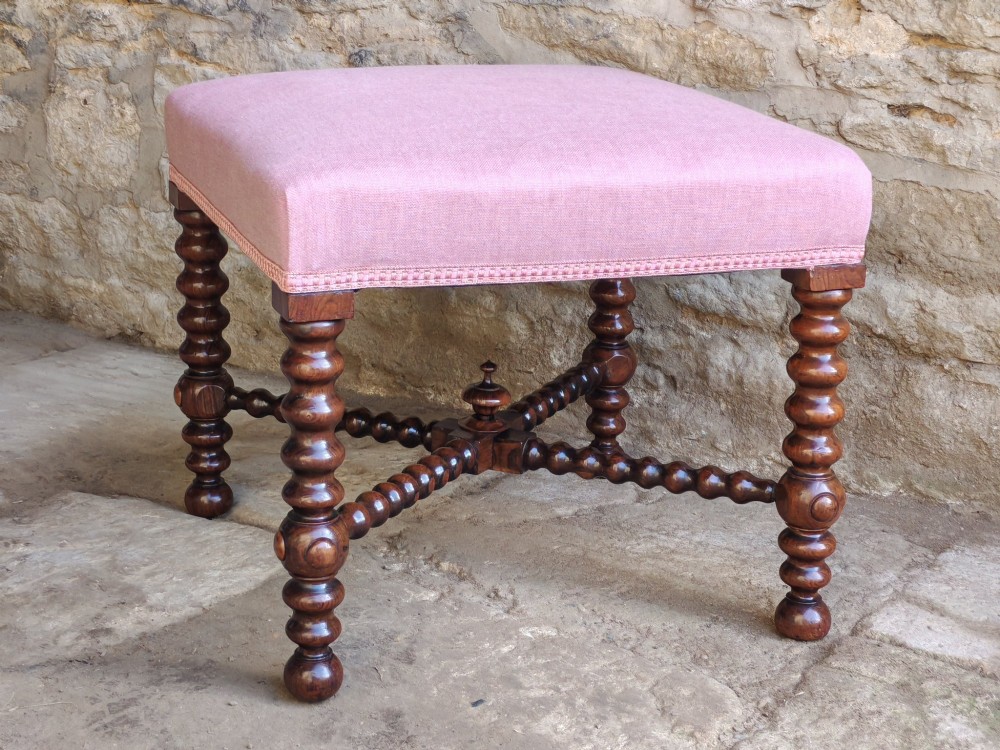 A Victorian rosewood stool featuring bobbin-turned legs, an X-shaped stretcher with a central finial, and a pink fabric upholstered seat.