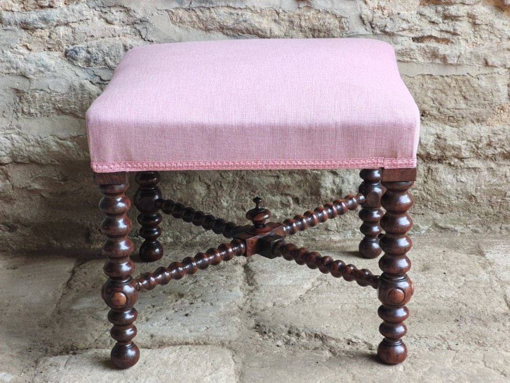 A Victorian rosewood stool featuring bobbin-turned legs, an X-shaped stretcher with a central finial, and a pink fabric upholstered seat. View II