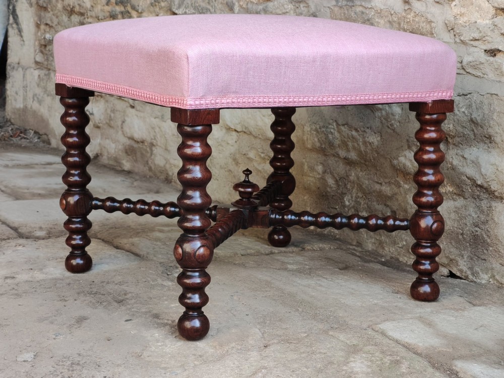 A Victorian rosewood stool featuring bobbin-turned legs, an X-shaped stretcher with a central finial, and a pink fabric upholstered seat. View VI