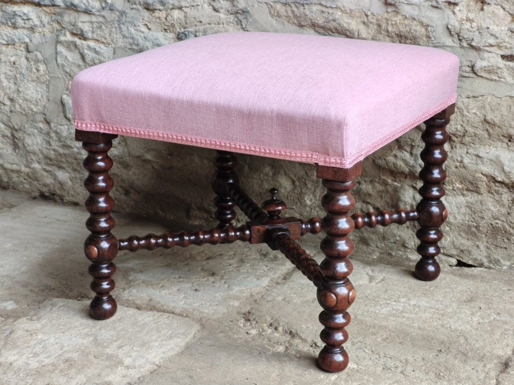 A Victorian rosewood stool featuring bobbin-turned legs, an X-shaped stretcher with a central finial, and a pink fabric upholstered seat. View VII