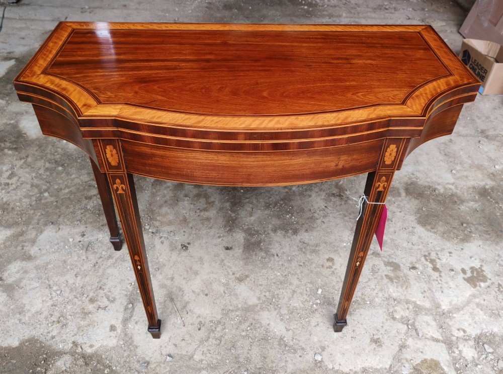 An antique late Victorian mahogany and satinwood fold-over tea table featuring a D-shaped top with satinwood crossbanding and tapered legs with floral marquetry.