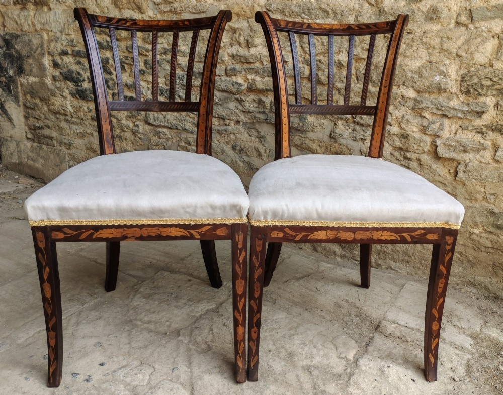 A pair of early 19th-century dark wood side chairs featuring floral marquetry inlay on the frames and light-coloured upholstered seats.