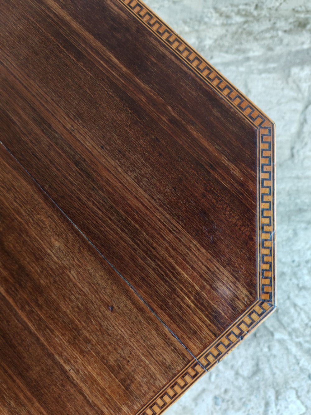 An octagonal dark mahogany Regency tilt-top table with central oval marquetry inlay, turned column, and splayed tripod legs. View IV