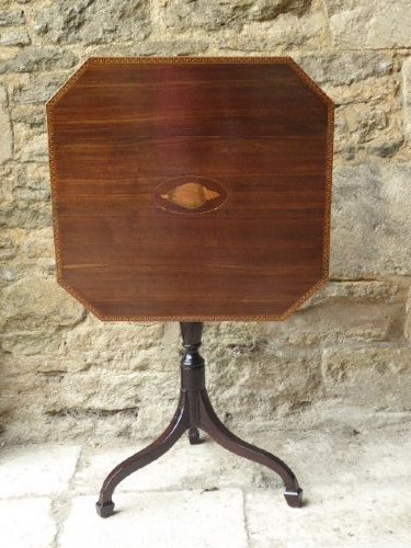 An octagonal dark mahogany Regency tilt-top table with central oval marquetry inlay, turned column, and splayed tripod legs. View VI