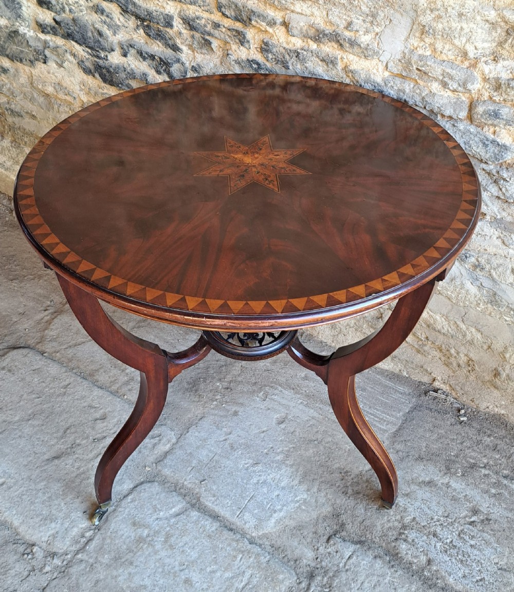 A circular mahogany occasional table featuring a central star inlay, geometric border, and sweeping sabre legs with brass castors.