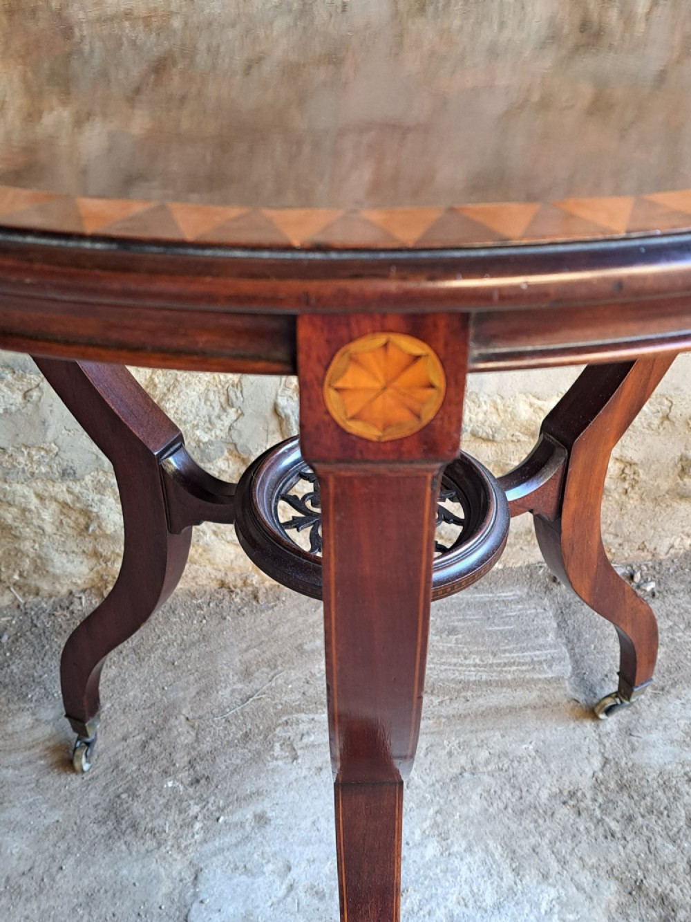 A circular mahogany occasional table featuring a central star inlay, geometric border, and sweeping sabre legs with brass castors. View V