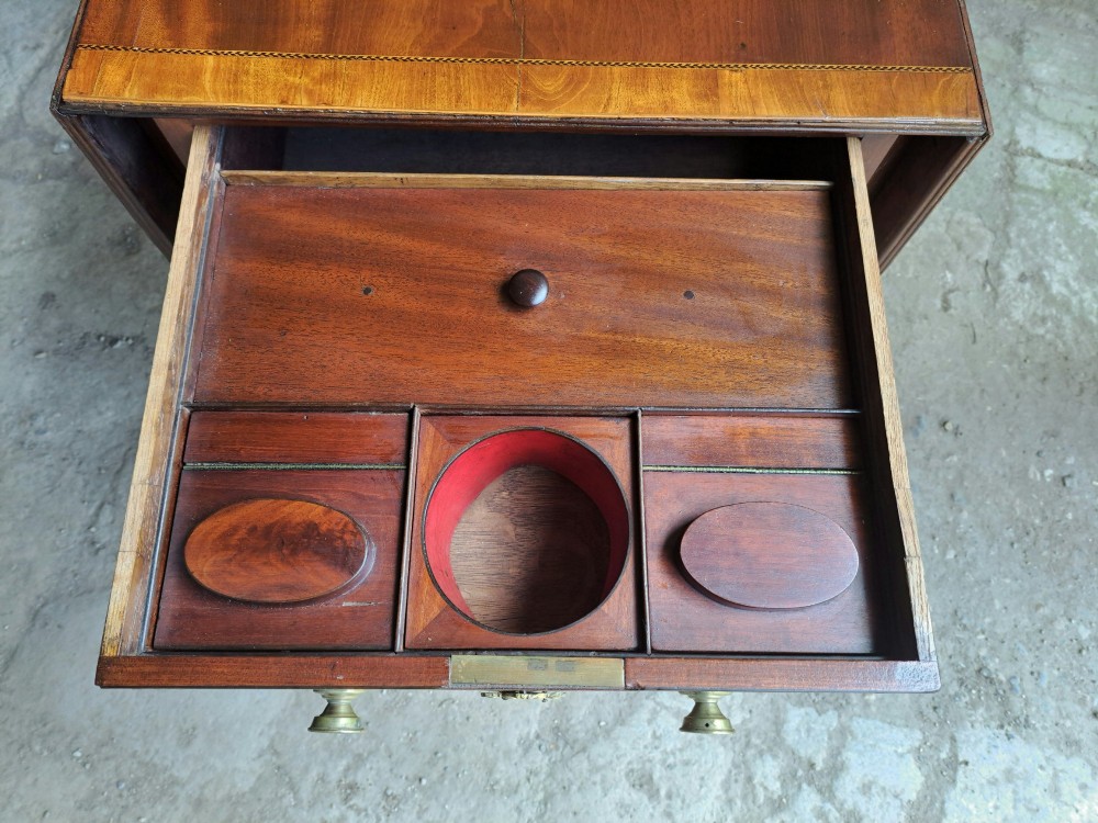 A Regency mahogany drop-leaf tea table featuring satinwood crossbanding, an oval marquetry motif, a single drawer with brass knobs, and splayed legs on castors. View II