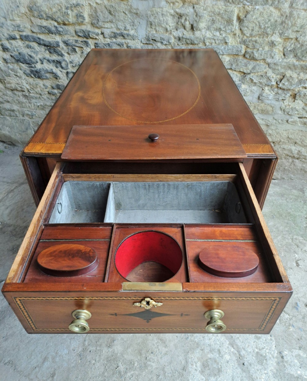 A Regency mahogany drop-leaf tea table featuring satinwood crossbanding, an oval marquetry motif, a single drawer with brass knobs, and splayed legs on castors. View III