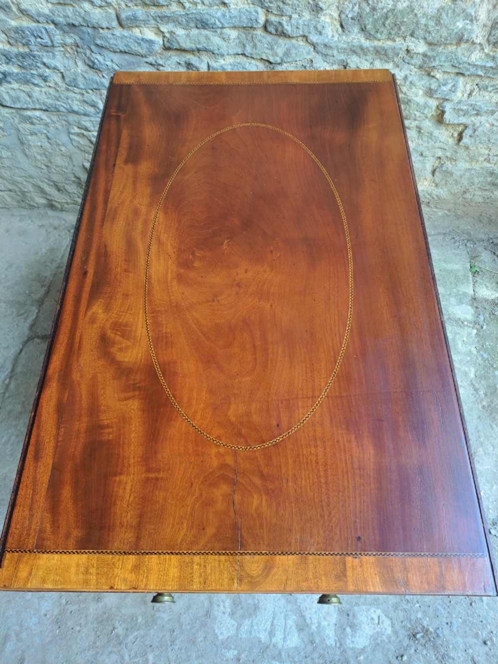 A Regency mahogany drop-leaf tea table featuring satinwood crossbanding, an oval marquetry motif, a single drawer with brass knobs, and splayed legs on castors. View VII