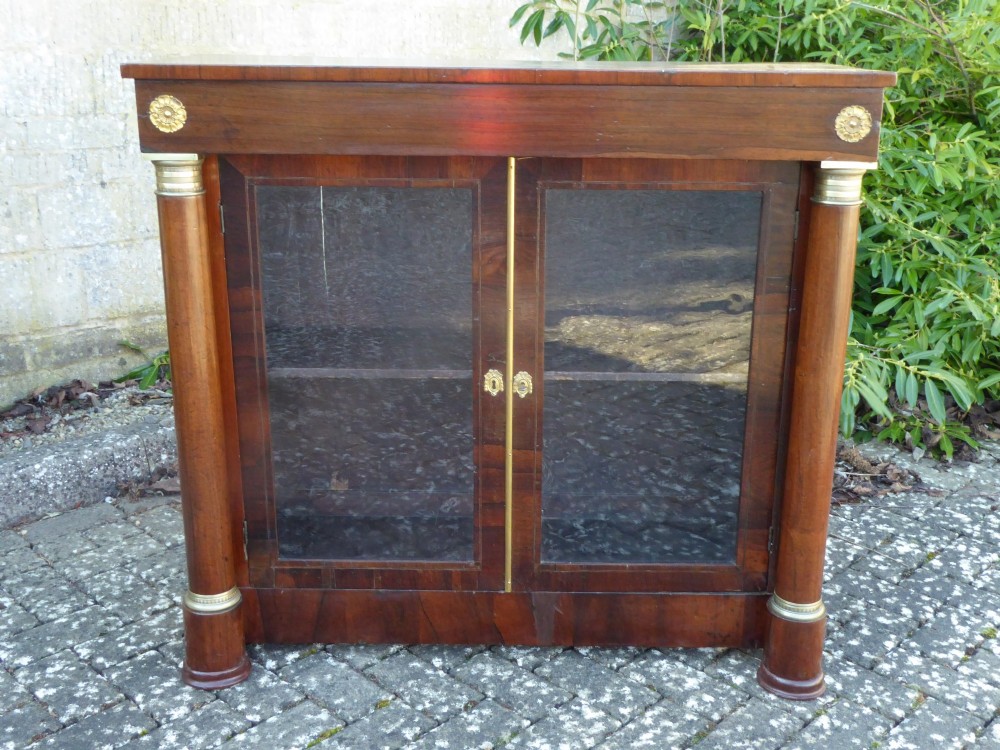 A low Regency rosewood bookcase featuring two glazed doors flanked by turned side columns with brass mounts.