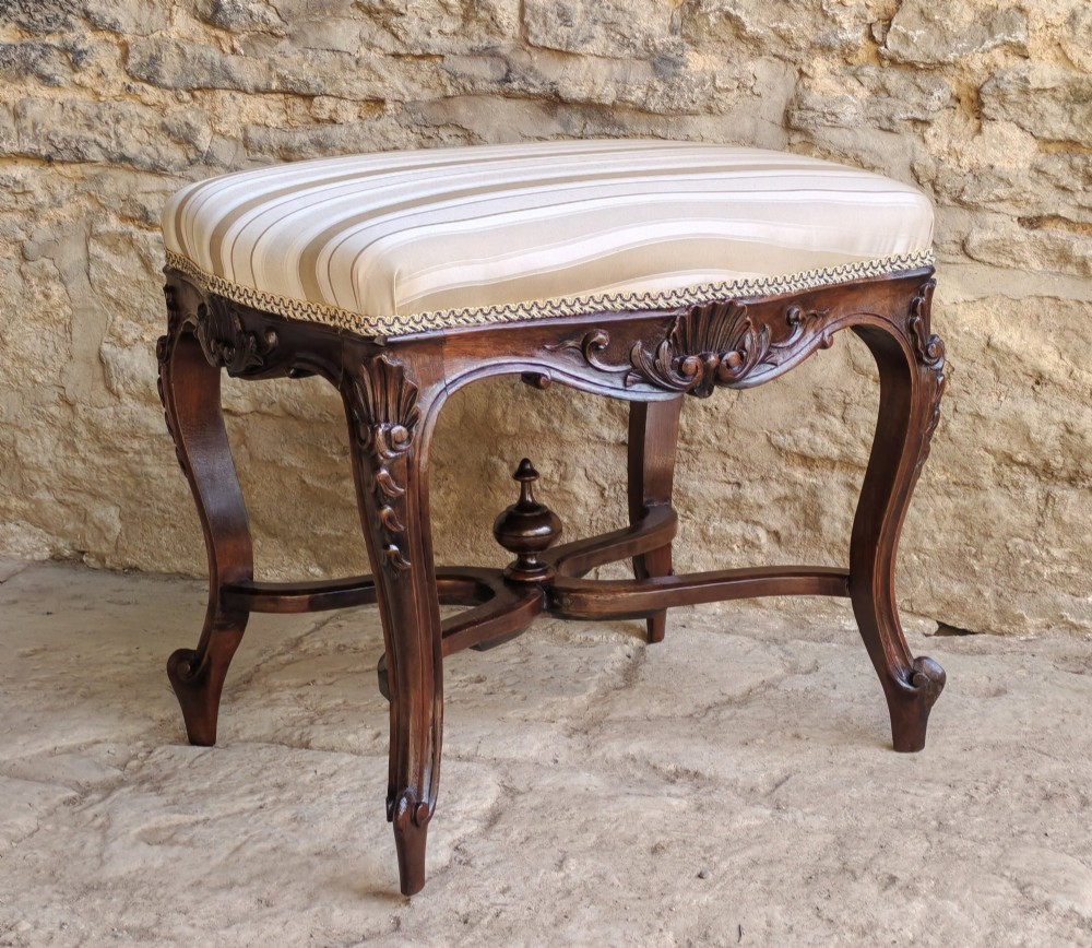 A carved dark mahogany Rococo style stool featuring a cream striped upholstered cushion, cabriole legs, carved shell motifs, and an X-stretcher with a turned finial. View II
