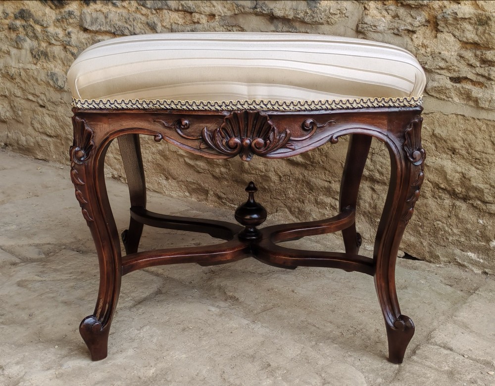 A carved dark mahogany Rococo style stool featuring a cream striped upholstered cushion, cabriole legs, carved shell motifs, and an X-stretcher with a turned finial. View VII