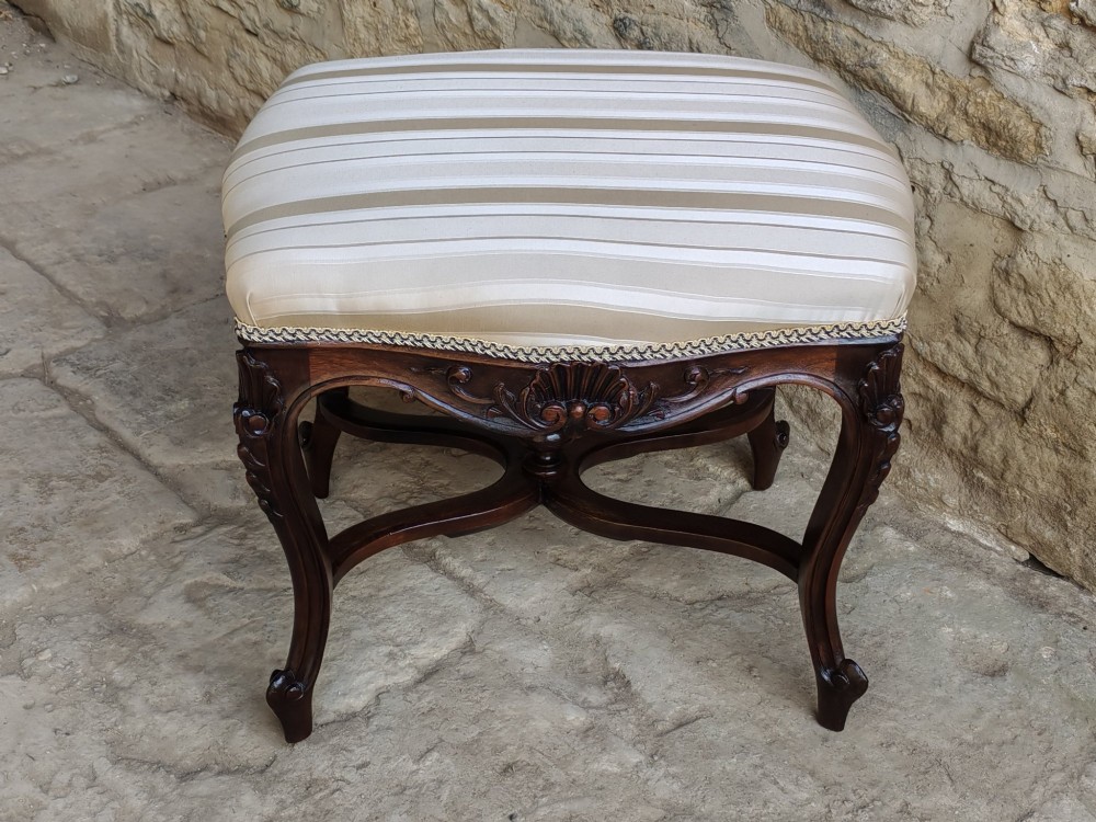 A carved dark mahogany Rococo style stool featuring a cream striped upholstered cushion, cabriole legs, carved shell motifs, and an X-stretcher with a turned finial. View VIII