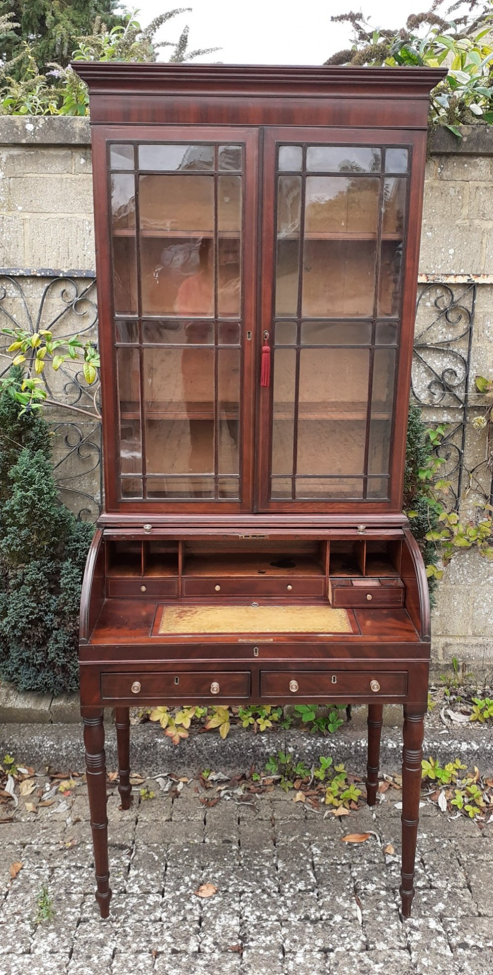An antique mahogany bureau bookcase with a glazed upper door cabinet resting on a cylinder roll-top writing desk with turned legs. View III