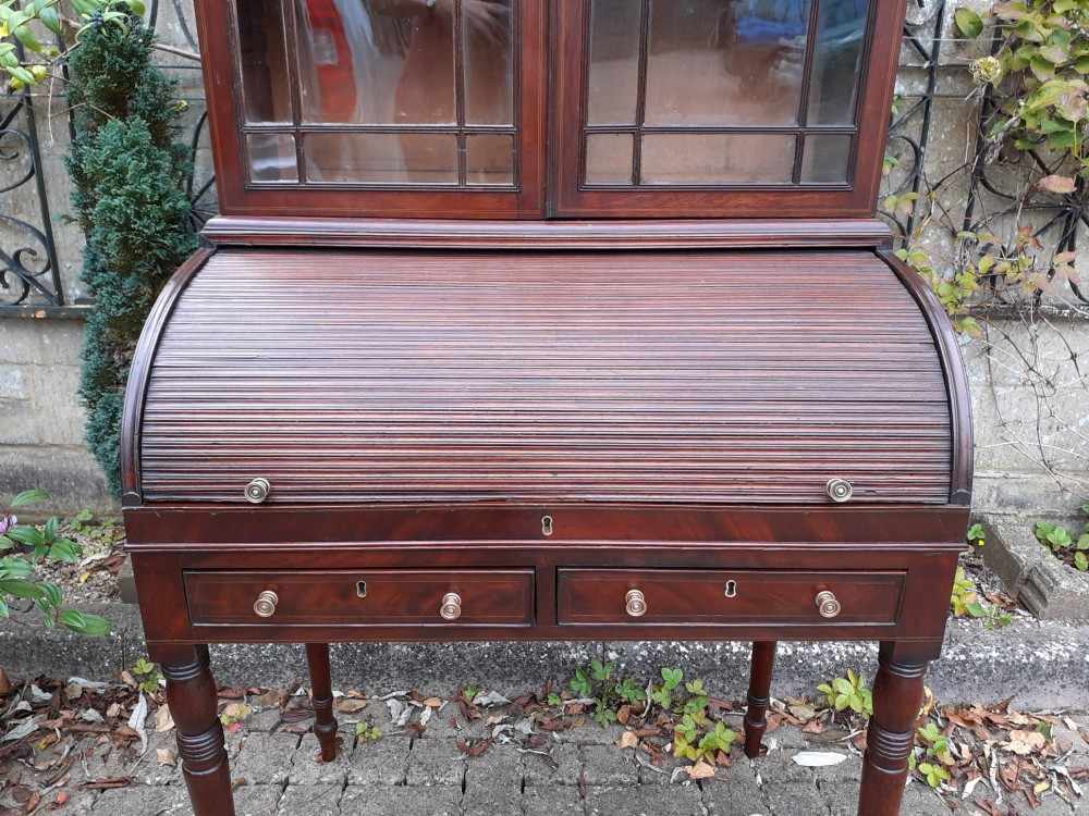 An antique mahogany bureau bookcase with a glazed upper door cabinet resting on a cylinder roll-top writing desk with turned legs. View IV