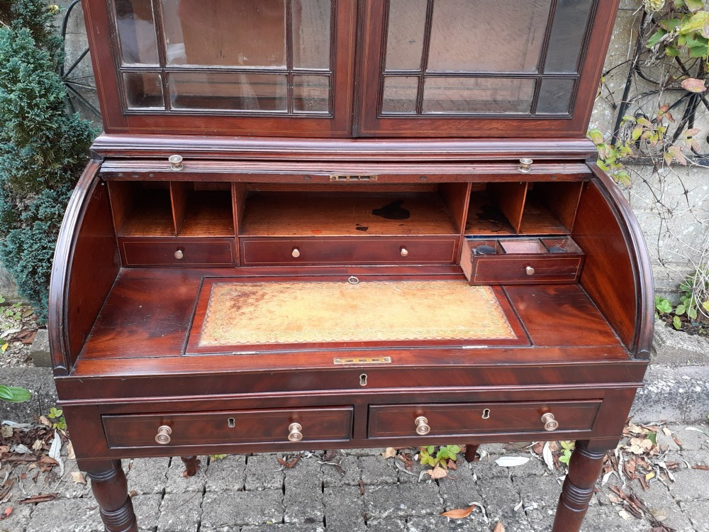 An antique mahogany bureau bookcase with a glazed upper door cabinet resting on a cylinder roll-top writing desk with turned legs. View V