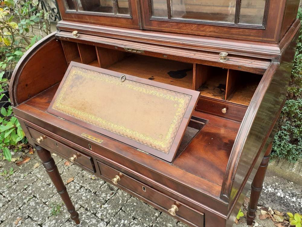 An antique mahogany bureau bookcase with a glazed upper door cabinet resting on a cylinder roll-top writing desk with turned legs. View VI