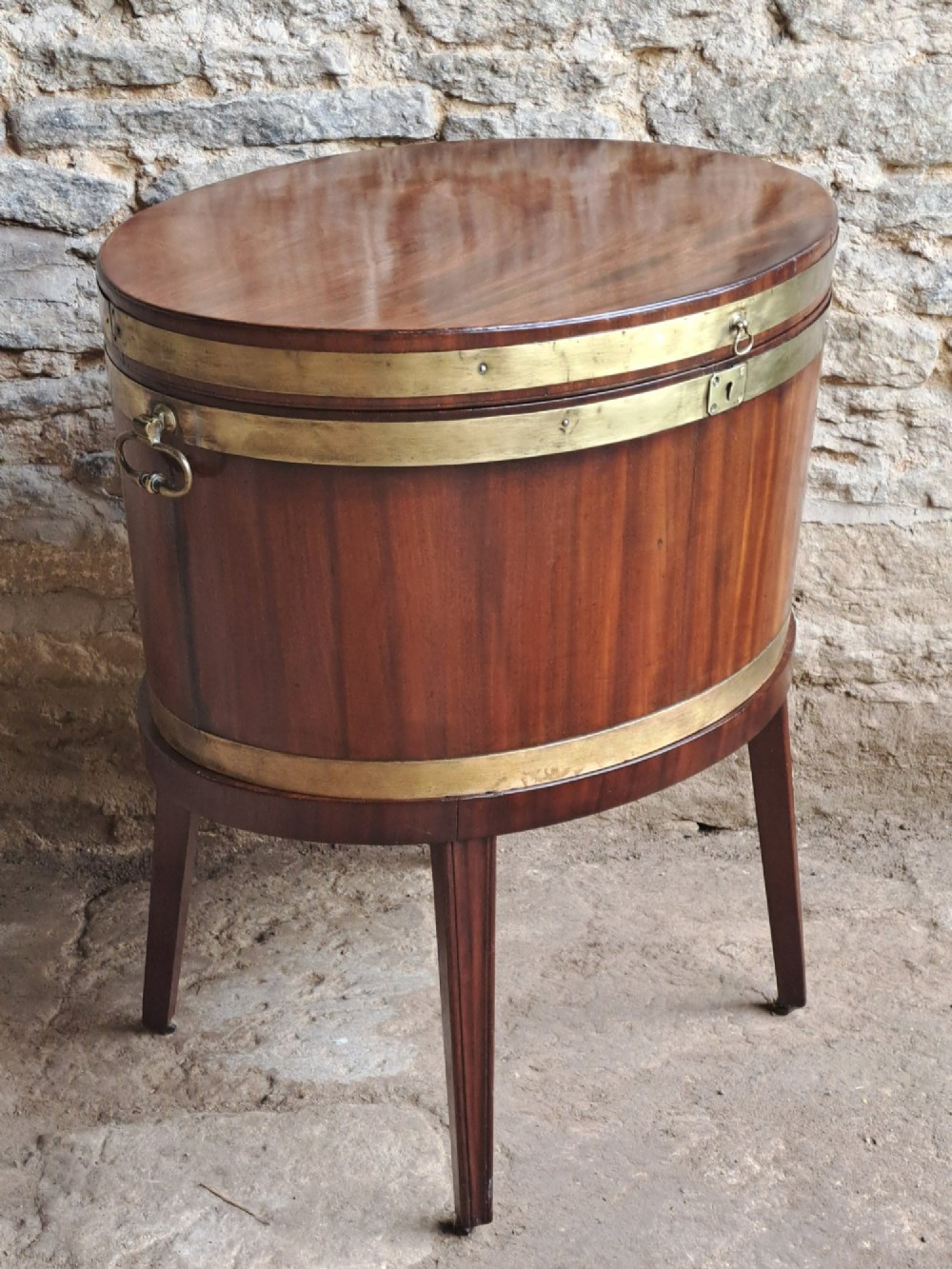 An 18th-century George III oval mahogany cellarette bound with brass straps and supported by four tapered legs. View II