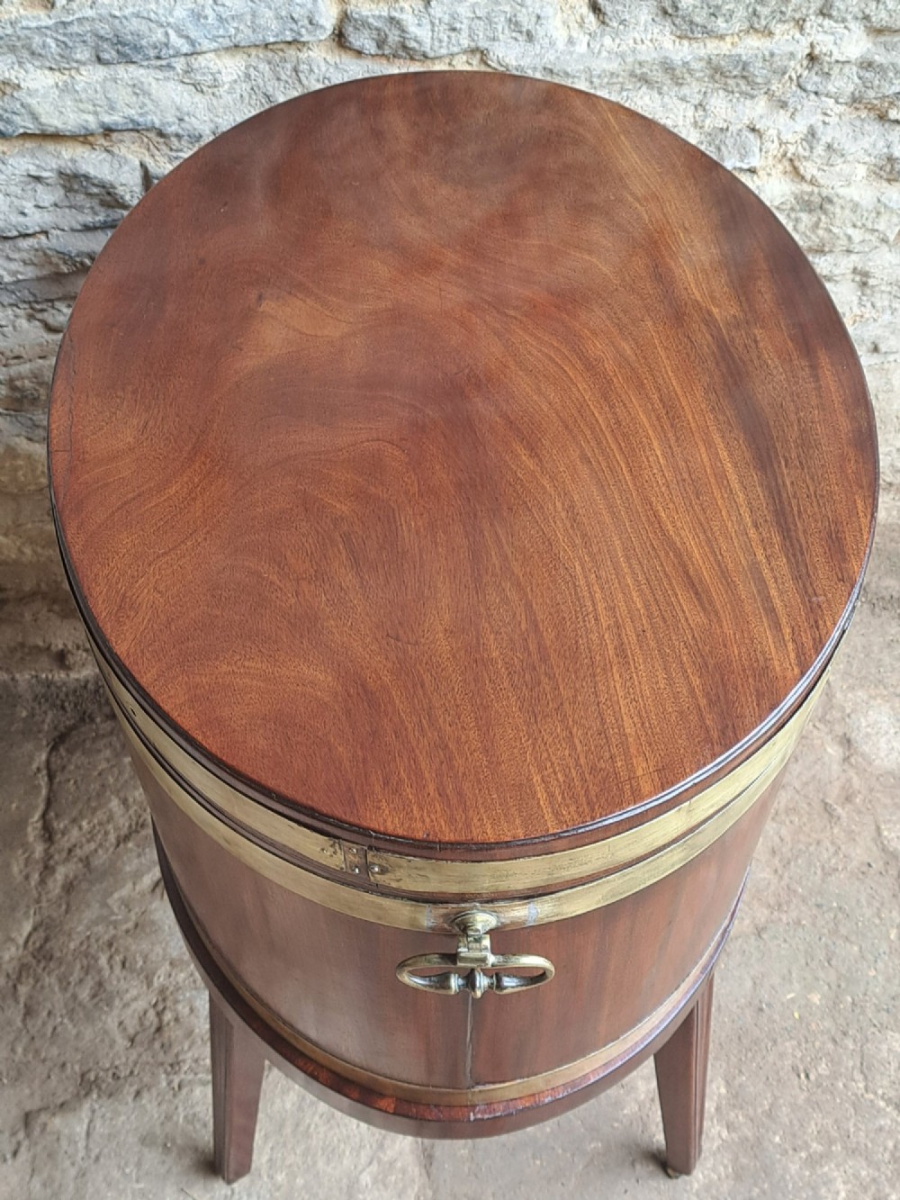 An 18th-century George III oval mahogany cellarette bound with brass straps and supported by four tapered legs. View III