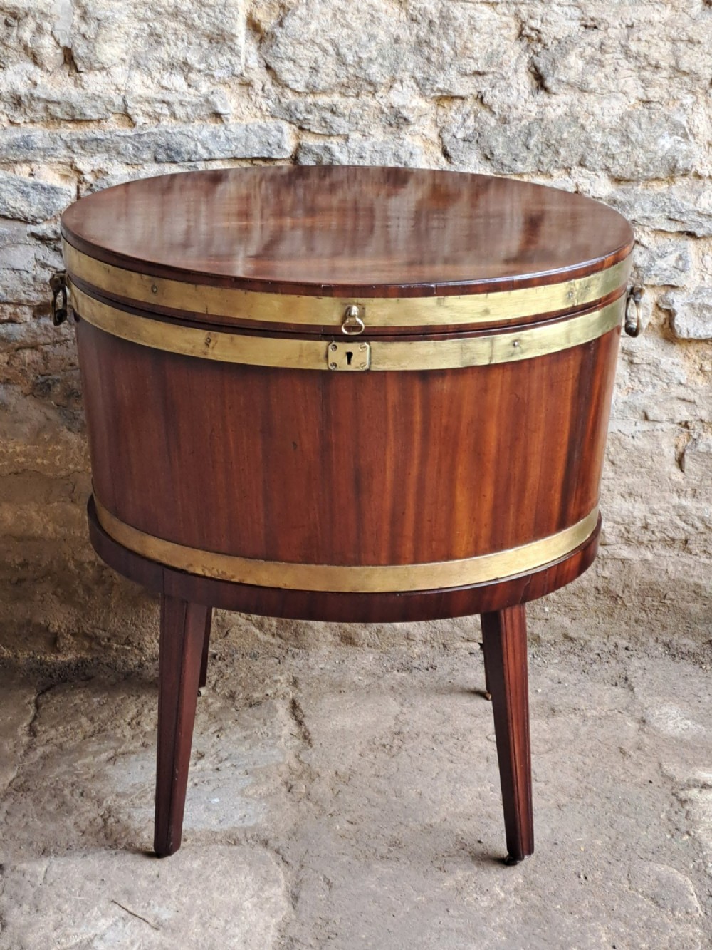An 18th-century George III oval mahogany cellarette bound with brass straps and supported by four tapered legs. View IV