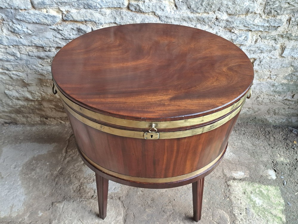 An 18th-century George III oval mahogany cellarette bound with brass straps and supported by four tapered legs. View V