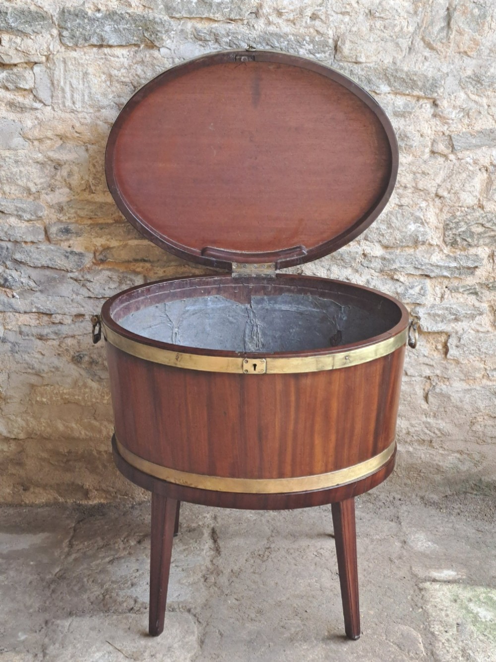 An 18th-century George III oval mahogany cellarette bound with brass straps and supported by four tapered legs. View VI
